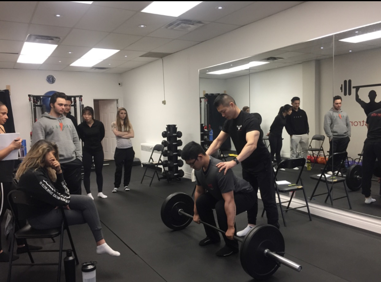 Min Moo (Steve) Lee coaching a deadlift while personal trainers observe